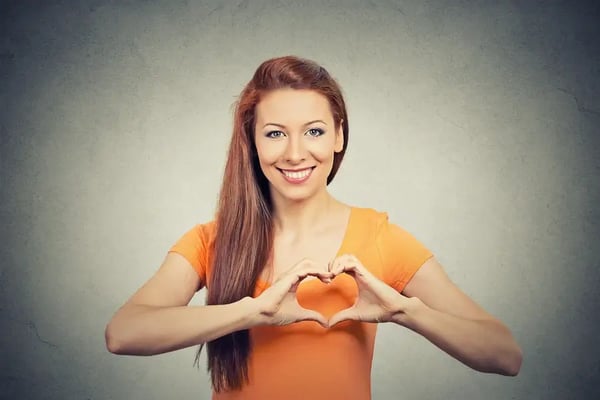 Closeup portrait smiling cheerful happy young woman making heart sign with hands isolated grey wall background. Positive human emotion expression feeling life perception attitude body language
