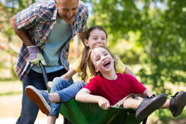 Happy father and his children playing with a wheelbarrow on a sunny day