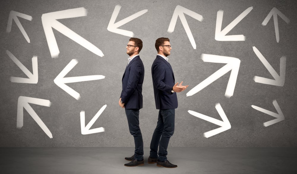 Young conflicted businessman choosing between two directions with arrows around him